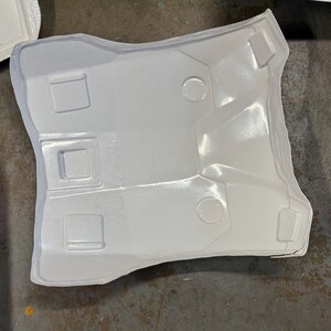 Puede incluir: Un componente de pl&aacute;stico moldeado blanco con forma curva y detalles geom&eacute;tricos. La pieza presenta tres hendiduras rectangulares y dos circulares, con una superficie texturizada. El art&iacute;culo parece ser parte de una estructura m&aacute;s grande.