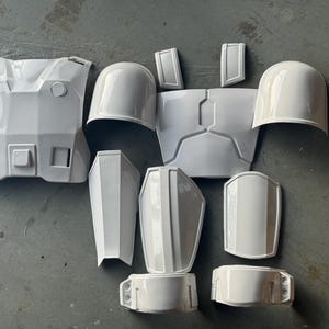 Puede incluir: Un conjunto de piezas de armadura de plástico blanco para cosplay o la elaboración de disfraces. Las piezas incluyen una placa de pecho, hombreras y protectores de brazos.