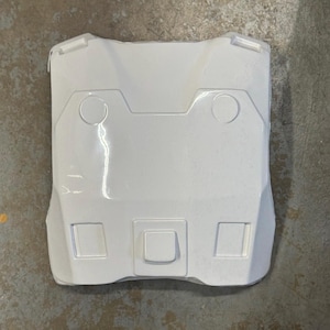 May include: A white, rectangular, plastic object with a series of geometric shapes. The object has two circular indentations near the top and three square indentations at the bottom. The overall shape is slightly curved.