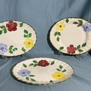 May include: Three oval ceramic plates with a white background and green, red, yellow and blue floral designs.