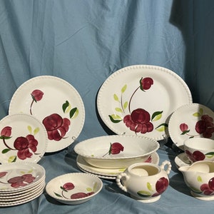 May include: A vintage floral dinner set featuring a white background with a red floral design. The set includes plates, bowls, a creamer, and a sugar bowl.