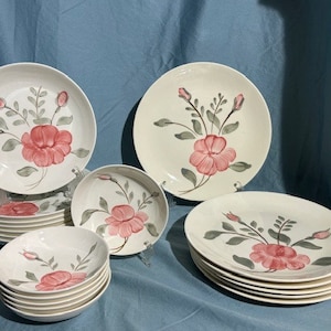 May include: A set of white ceramic dinnerware with a floral design featuring pink roses and green leaves. The set includes dinner plates, salad plates, and bowls.