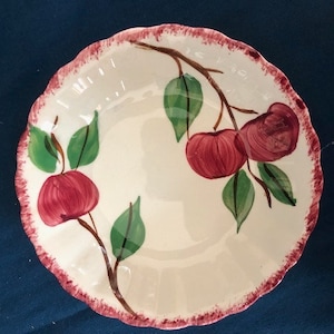 May include: A white ceramic bowl with a scalloped edge and a pink rim. The bowl features a hand-painted design of red apples and green leaves on a branch.