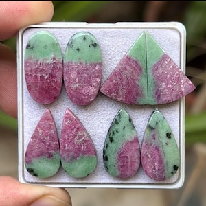 Op de afbeelding: Assortiment van zes groene en roze edelsteen cabochons, waaronder twee druppelvormen, twee ovale vormen en twee halve maanvormen.