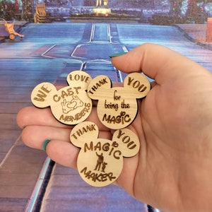 May include: Four wooden Mickey Mouse head ornaments with different messages. The first says "We Love Cast Members". The second says "Thank You for being the Magic". The third says "Thank You Magic Maker".