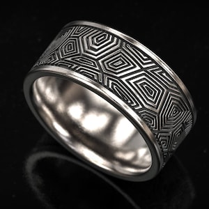 Könnte beinhalten: Ein silberner Ring mit geometrischem Muster. Der Ring hat ein sich wiederholendes Design aus miteinander verbundenen Formen um das Band. Der Ring besteht aus glänzendem Metall und ist vor einem dunklen Hintergrund platziert.
