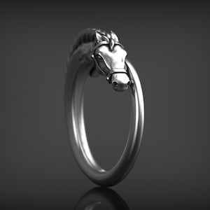 May include: A silver-colored ring featuring a horse head design. The horse head is detailed with a bridle and mane, and the ring band forms a complete circle. The ring is set against a dark background.