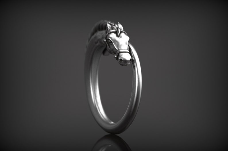May include: A silver-colored ring featuring a horse head design. The horse head is detailed with a bridle and mane, and the ring band forms a complete circle. The ring is set against a dark background.