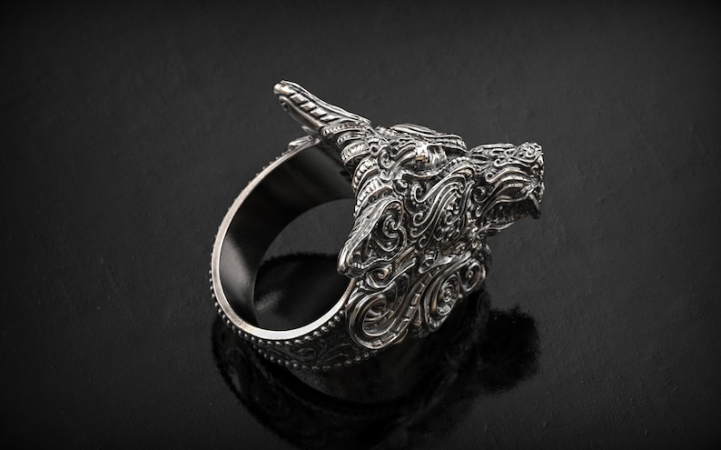 May include: A silver-colored ring featuring a detailed dragon head design. The dragon's head is intricately carved with scales, horns, and facial features. The ring has a wide band and is displayed against a dark background.