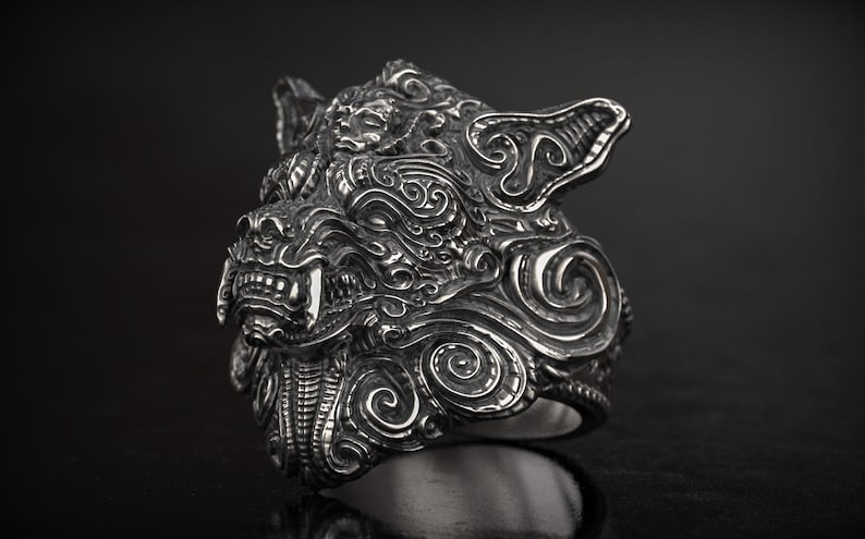May include: A detailed silver ring featuring a stylized wolf's head with intricate carvings. The ring showcases sharp teeth and a textured surface, set against a dark background. The design is bold and eye-catching.