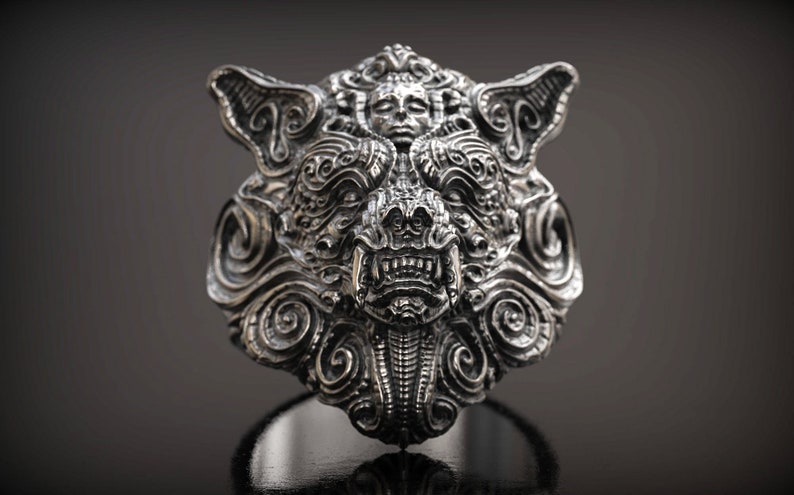 May include: A detailed silver ring featuring a stylized wolf's head design. The ring showcases intricate carvings, including a central face with bared teeth and swirling patterns. The ring is displayed against a dark background.