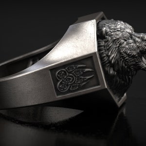 May include: A silver-colored ring featuring a detailed bear head design. The ring has a rectangular accent with a claw symbol. The bear's mouth is open, and the ring is set against a dark background.