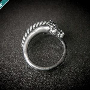 May include: A silver-toned ring featuring a horse head design. The horse head is detailed with a bridle and mane, and the ring band has a rope-like texture. The ring is set against a dark background.
