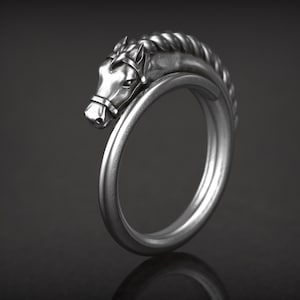 May include: A silver-colored ring featuring a horse head design. The horse head is detailed with a bridle and a braided mane. The ring curves around to form a complete circle.