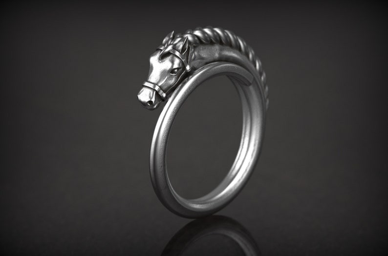 May include: A silver-colored ring featuring a horse head design. The horse head is detailed with a bridle and a braided mane. The ring curves around to form a complete circle.