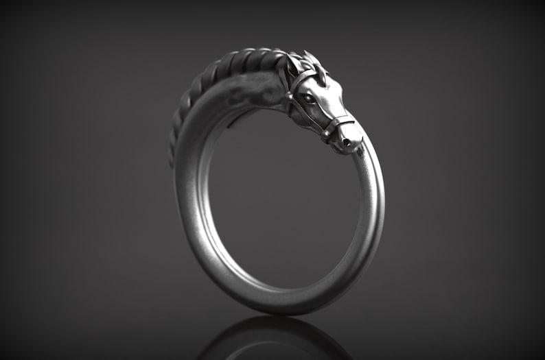 May include: A silver-colored ring featuring a horse head design. The horse head is detailed with a bridle and mane, and the ring forms a continuous loop. The ring is set against a dark gray background.