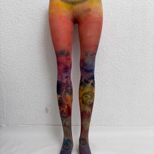Könnte beinhalten: Transparente Strumpfhose mit einem lebendigen Farbverlauf in Gelb, Orange, Rot und Violett. Der Stoff zeigt ein dunkles kreisförmiges Symbol an der Taille und kleinere passende Symbole an den Knöcheln, überlagert von einem abstrakten Druck.