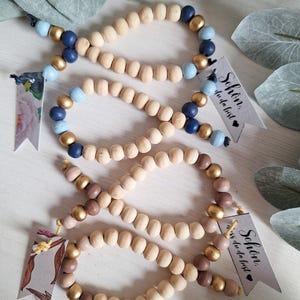 Könnte beinhalten: Drei Holzperlenarmbänder mit goldenen und blauen Perlen. Die Armbänder sind mit einer Schnur gebunden und haben ein kleines Schild mit der Aufschrift "Schön, dass du da bist", was übersetzt "Schön, dass du da bist" bedeutet.