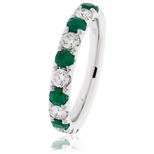 May include: A white gold ring with alternating emerald and diamond stones. The ring features a row of round, vibrant green emeralds and sparkling white diamonds set in a polished band. The ring is a classic design.