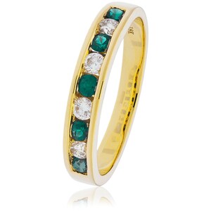 May include: A gold band ring with alternating emerald green and clear gemstones. The ring has a channel setting, with the gemstones set flush within the band. The ring is made of 18K gold.
