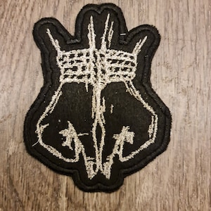 May include: Black embroidered patch with a white design of two hands clasped together with a crown on top.