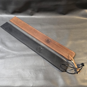 May include: Two leather straps, one black and one brown, with decorative stitching and a circular design. The straps are laid out on a gray surface.