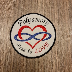 Puede incluir: Un parche blanco bordado con un corazón rojo y un símbolo de infinito azul. El texto "Polyamory Free to LOVE" está bordado alrededor del corazón y el símbolo de infinito.