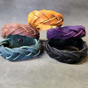 Könnte beinhalten: Vier geflochtene Lederarmbänder in verschiedenen Farben: Braun, Türkis, Lila und Schwarz. Die Armbänder sind alle mit dem gleichen geflochtenen Muster gefertigt.
