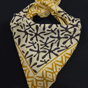 May include: A cream-coloured bandana with a black and yellow geometric pattern. The bandana is folded and tied in a knot.