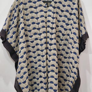 May include: A beige and blue patterned caftan with a V-neck and short sleeves. The fabric features a repeating fan-like design in navy blue. The edges of the sleeves and neckline are trimmed with a dark brown fabric.