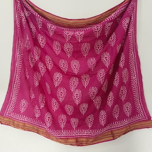 May include: A magenta scarf with a white feather pattern. The scarf has a gold border with a detailed design. The fabric is lightweight and appears to be draped. The scarf is a square shape.
