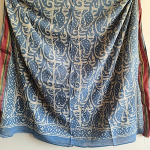 Könnte beinhalten: Blau-weißes Textil mit einem sich wiederholenden Muster aus stilisierten Blättern und Punkten. Die Ränder weisen einen Rand aus roten, gelben und grünen Streifen auf. Der Stoff ist drapiert und zeigt seine Textur und sein Muster.