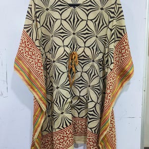 May include: A beige kaftan with a black floral pattern and red and yellow patterned trim. The kaftan has a drawstring waist and wide sleeves. The fabric appears lightweight and suitable for warm weather. The garment is hanging on a black hanger.