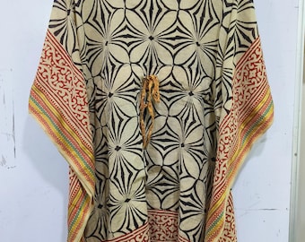 May include: A beige kaftan with a black floral pattern and red and yellow patterned trim. The kaftan has a drawstring waist and wide sleeves. The fabric appears lightweight and suitable for warm weather. The garment is hanging on a black hanger.