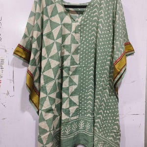 May include: A green and white cotton kaftan with a geometric print and gold trim. The kaftan has a V-neck and short sleeves.