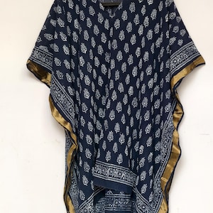 May include: A navy blue caftan with a white leaf pattern and gold trim. The caftan has a V-neck and wide sleeves. The fabric appears to be lightweight and suitable for warm weather.