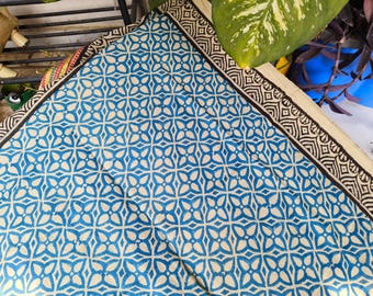 May include: A white fabric with a blue and brown geometric pattern. The fabric has a border with a brown and white geometric pattern.