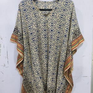 May include: A beige, loose-fitting kaftan with a geometric pattern in navy blue and black. The sleeves and hem are trimmed with a colorful striped border. The kaftan is hanging on a black hanger.