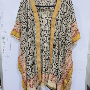 May include: A beige, black, and red patterned kimono-style garment with gold trim. The open-front design features a geometric and floral print. The garment is hanging on a black hanger against a white background.
