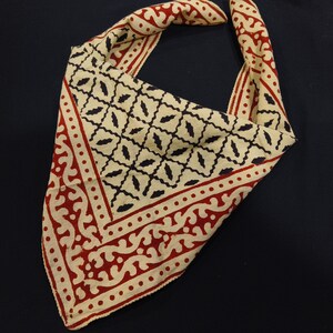 May include: A cream-colored bandana with a red and black geometric pattern. The bandana has a paisley-like border.