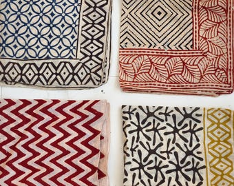 May include: Four folded fabric squares with different printed patterns. One has a blue and white floral design, another has a black and red geometric pattern, a third has a red zigzag pattern, and the last has a black and yellow starburst design.