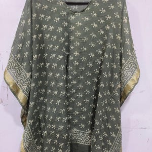 May include: A green, loose-fitting kaftan with a V-neck and short sleeves. The fabric features a repeating pattern of small, off-white leaf-like shapes. The edges are trimmed with a gold border and a patterned design.