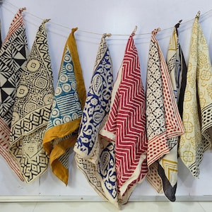 Könnte beinhalten: Eine Sammlung von acht handbedruckten Baumwollschals in verschiedenen Farben mit geometrischen und floralen Mustern. Die Schals hängen an einer weißen Wand und sind alle in unterschiedlichen Größen und Formen.