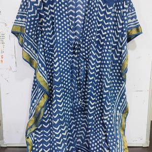 May include: A blue and white patterned kaftan with a V-neck and short sleeves. The fabric features a repeating pattern of white dots and chevron shapes. Gold trim accents the edges of the sleeves and hem.