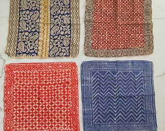 May include: Four square patterned textiles. The textiles feature various designs, including paisley, floral, and geometric patterns. Colors include navy blue, red, and cream. The textiles are arranged on a white surface.