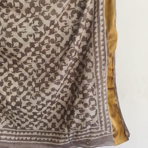 Puede incluir: Un textil drapeado con un patr&oacute;n floral repetitivo en tonos marr&oacute;n y beige. La tela tiene un borde con un dise&ntilde;o geom&eacute;trico y un ribete dorado a lo largo de un borde. El textil es probablemente una bufanda o chal.