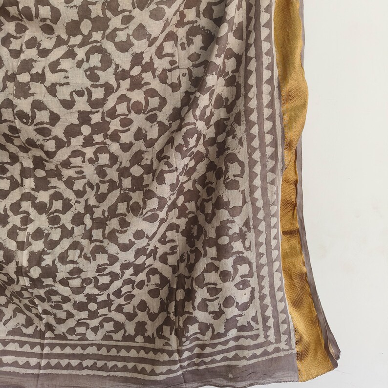 Puede incluir: Un textil drapeado con un patr&oacute;n floral repetitivo en tonos marr&oacute;n y beige. La tela tiene un borde con un dise&ntilde;o geom&eacute;trico y un ribete dorado a lo largo de un borde. El textil es probablemente una bufanda o chal.