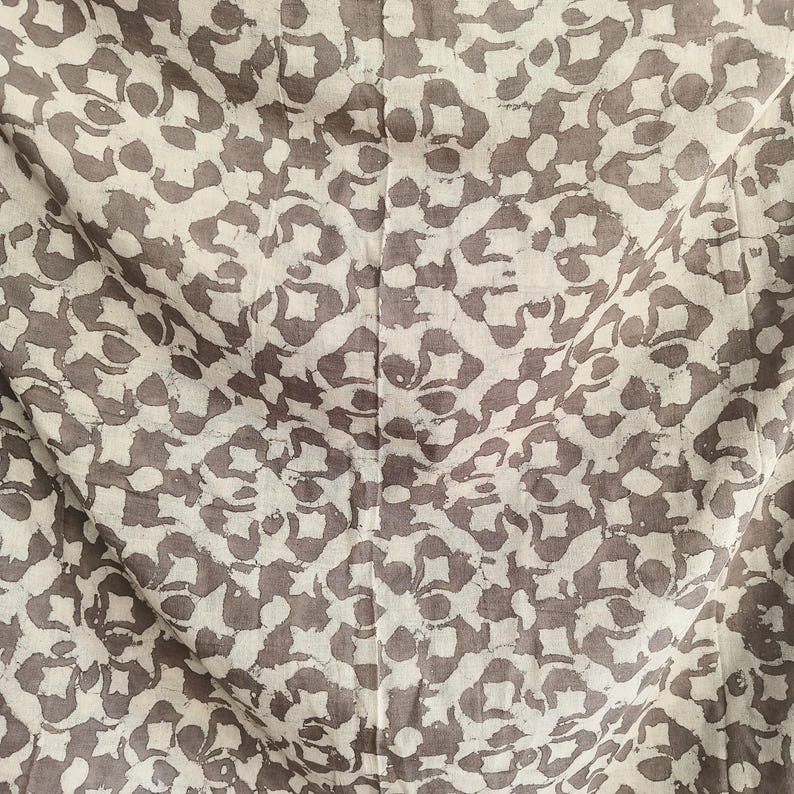 Puede incluir: Primer plano de una tela con un patr&oacute;n repetitivo. El dise&ntilde;o presenta un fondo beige claro con un patr&oacute;n de formas florales de color topo. La tela est&aacute; ligeramente arrugada, con una costura vertical visible en el centro.