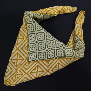 May include: A yellow and green patterned bandana with a geometric design. The bandana is folded into a triangle shape.