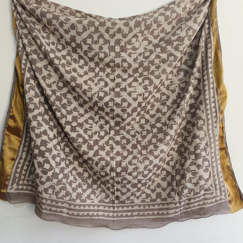 Puede incluir: Bufanda drapeada con un estampado floral repetido en tonos marr&oacute;n y beige. La bufanda tiene un borde con dise&ntilde;o geom&eacute;trico y un ribete dorado. La tela parece suave y fluida.